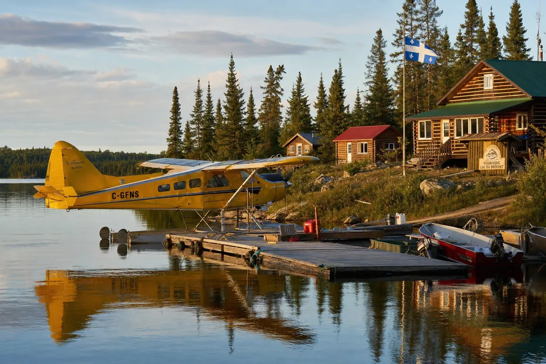 Yellow float plane docked at a remote Québec outfitter lodge with log cabins and fishing boats
